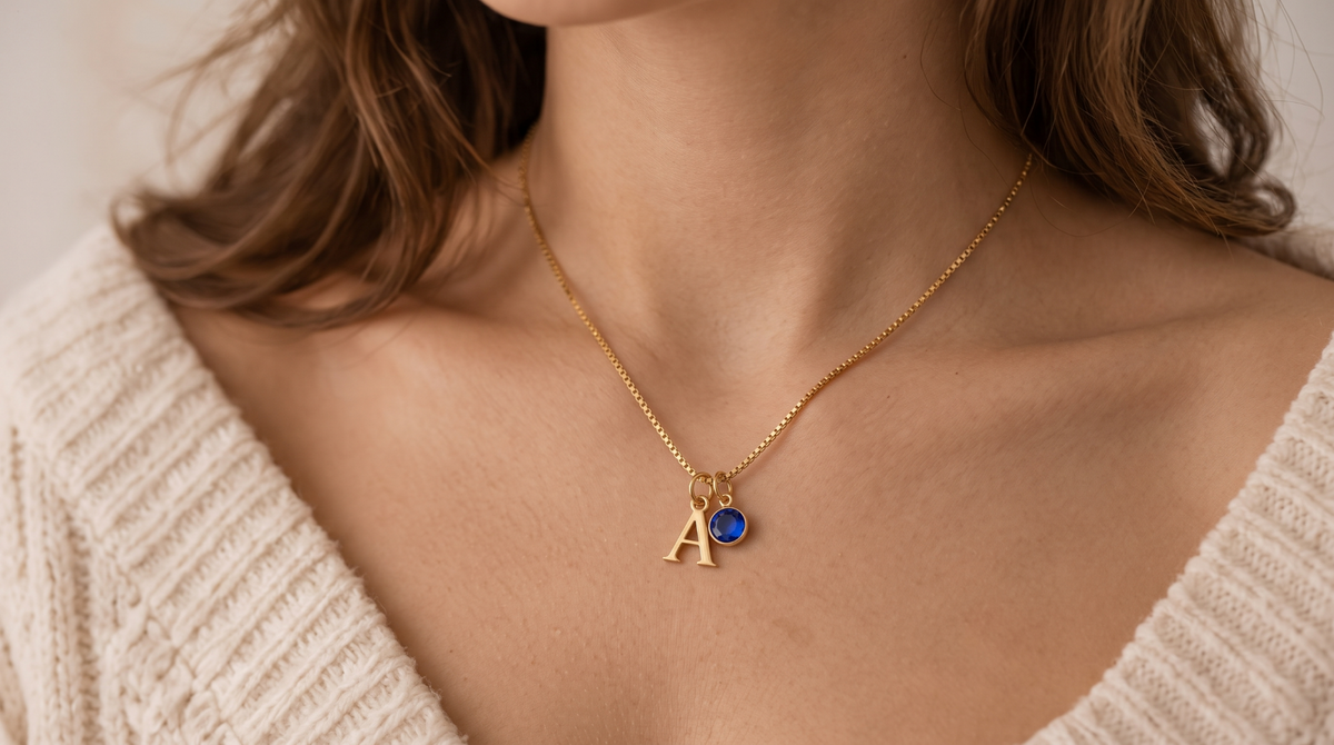 Close-up of gold initial and blue birthstone necklace worn at the collarbone